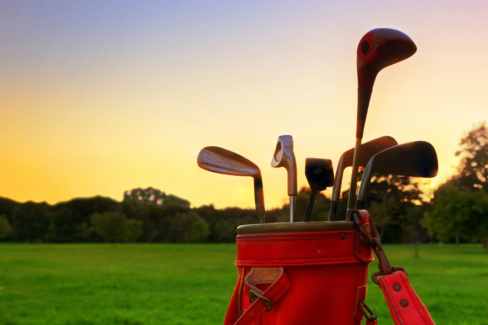 A red bag of golf clubs sitting on top of the grass.