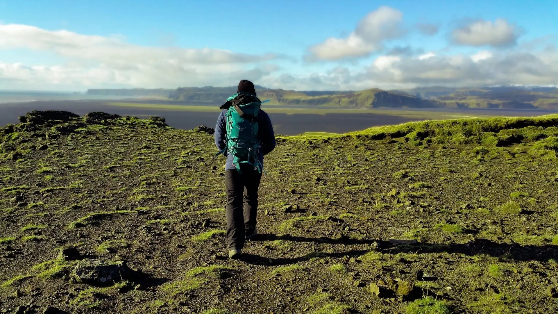 A person with a backpack walking on the side of a hill.