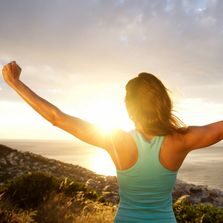 A woman standing on top of a hill with her arms in the air.